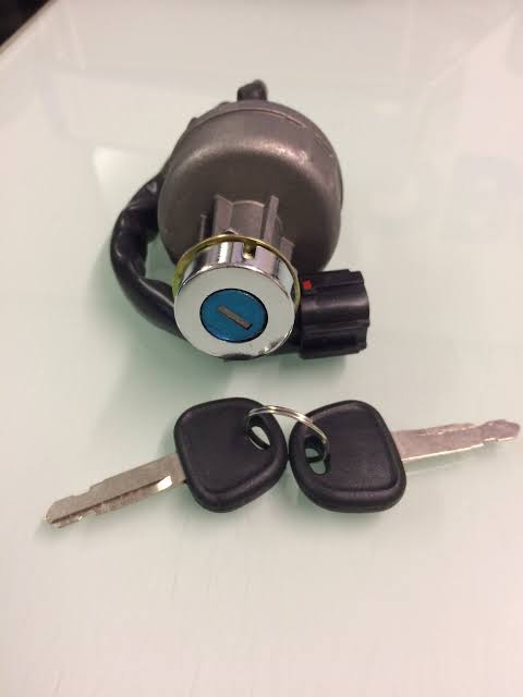 A metal ignition switch for heavy machinery with a blue keyhole and two black plastic-headed keys attached to a ring.