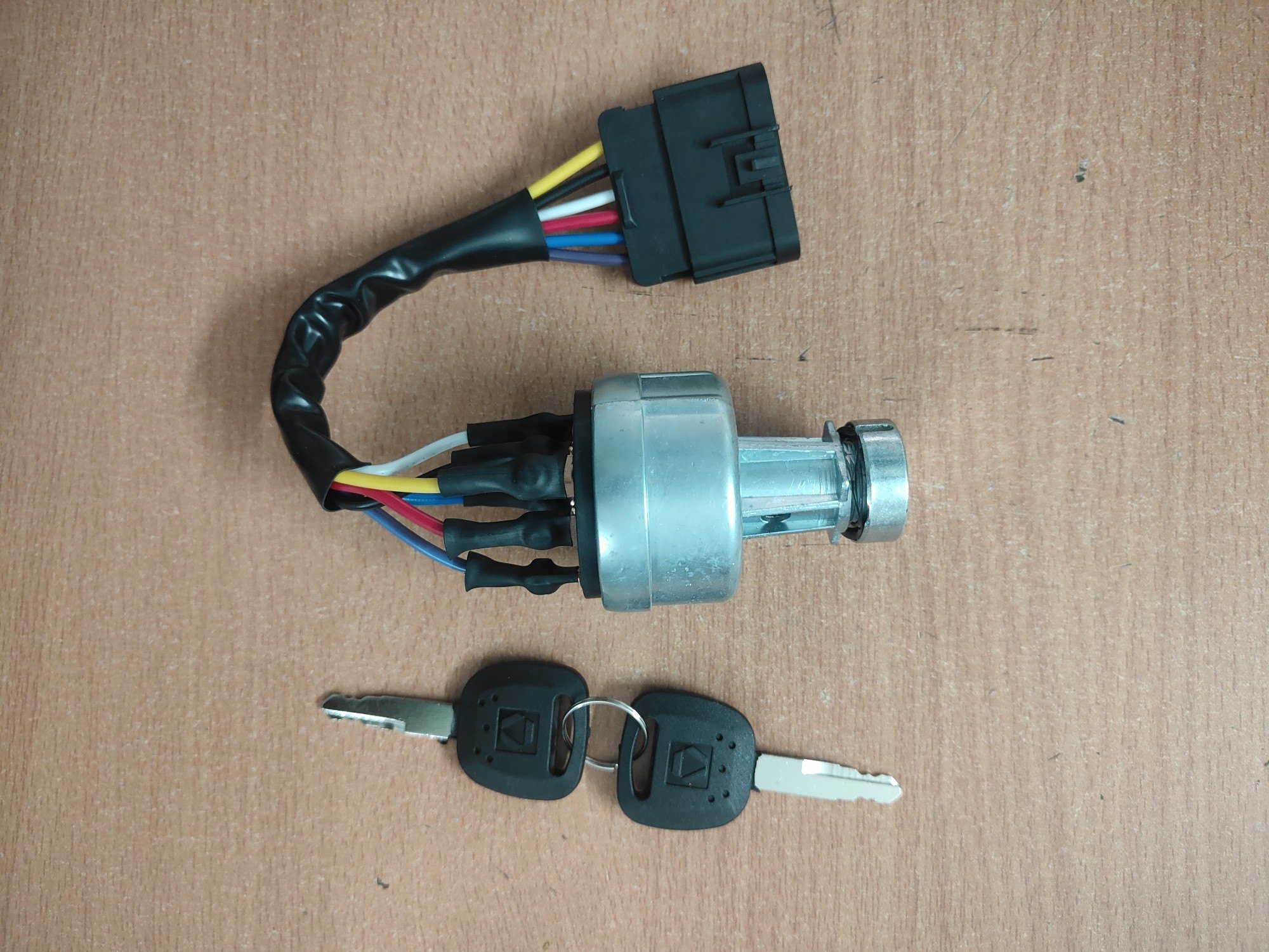 A metal ignition switch for heavy machinery with a multi-wire harness and two matching black keys.